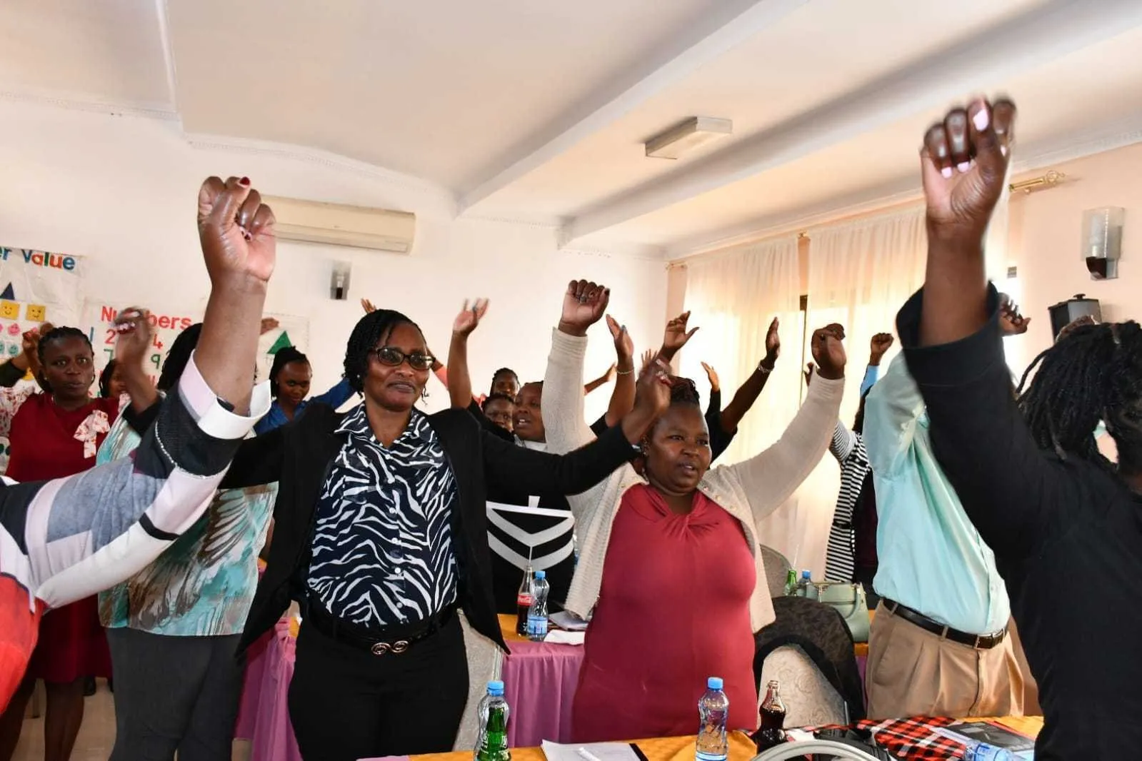 Teachers standing with their arms raised during an energiser at a training workshop
