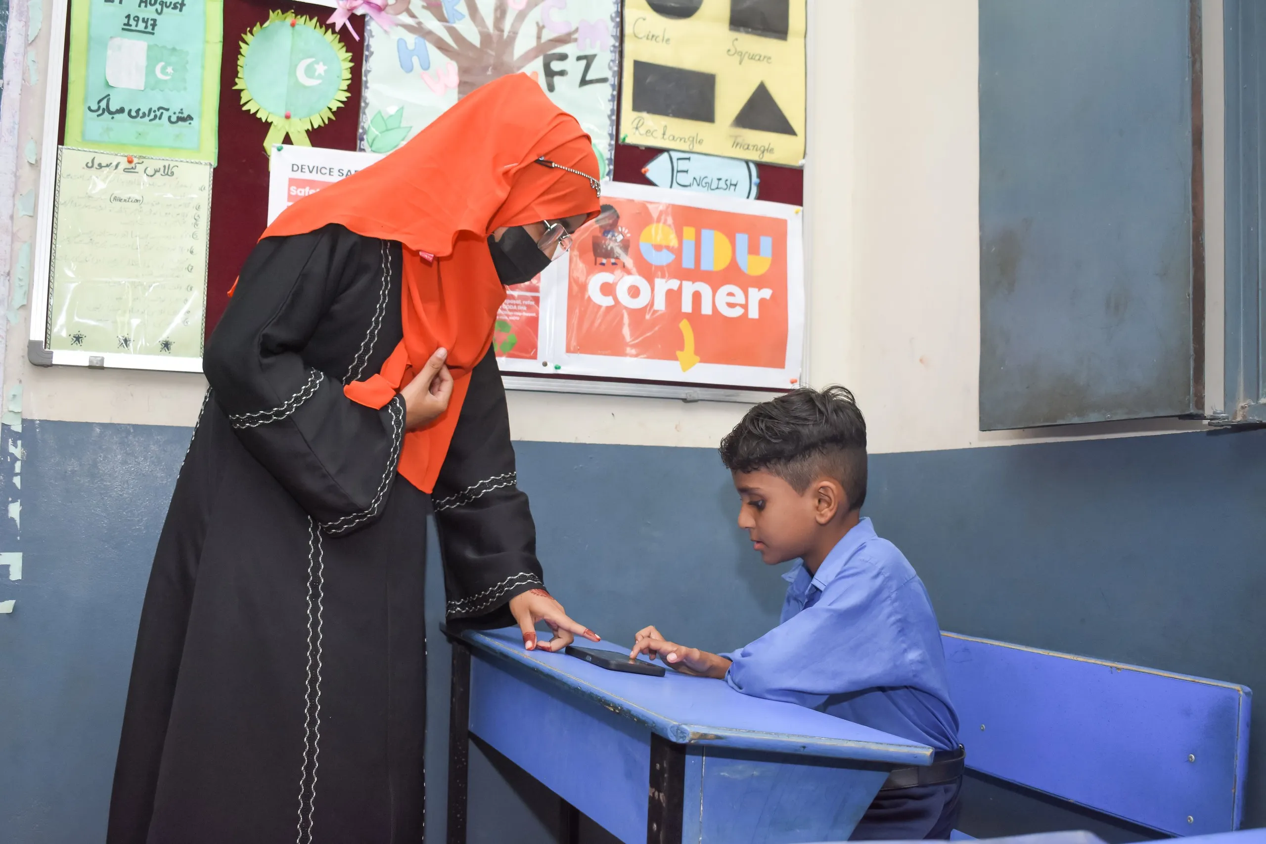 Teacher guiding a boy through a lesson on a phone at a desk in the EIDU Corner