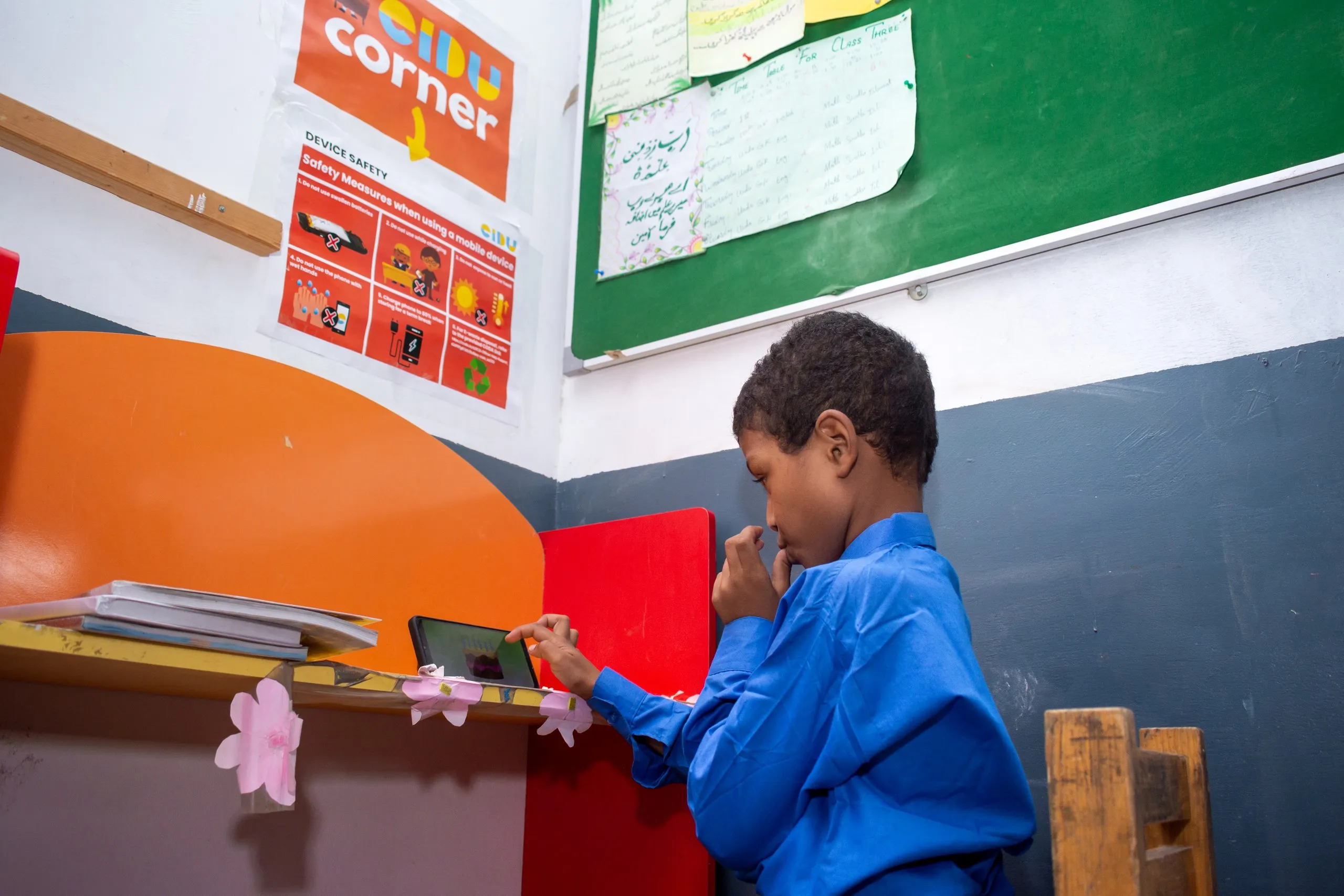 Boy in a blue uniform doing a lesson on a phone in the EIDU Corner, under a device safety poster