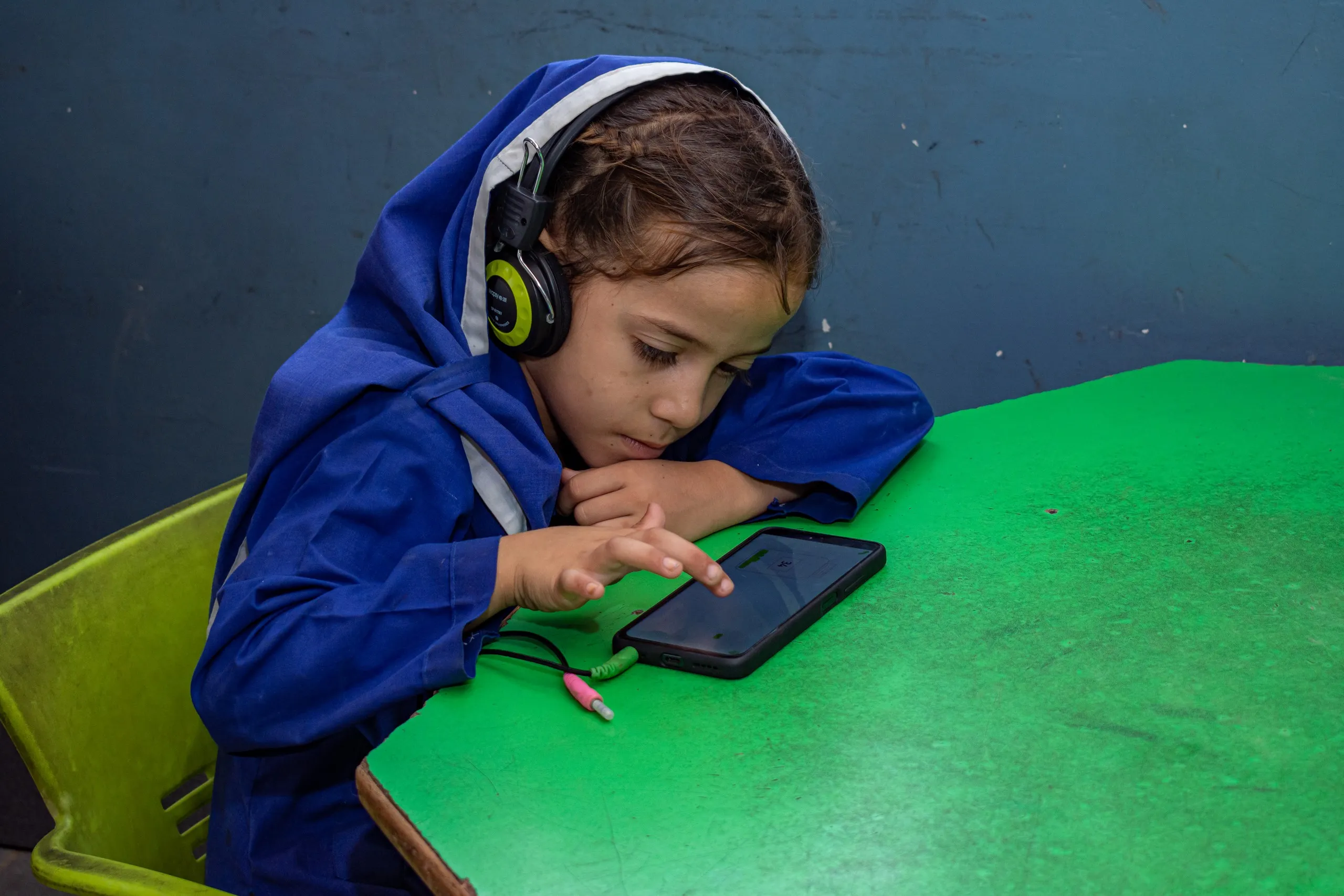Girl in a blue school uniform and headphones doing a lesson on a phone