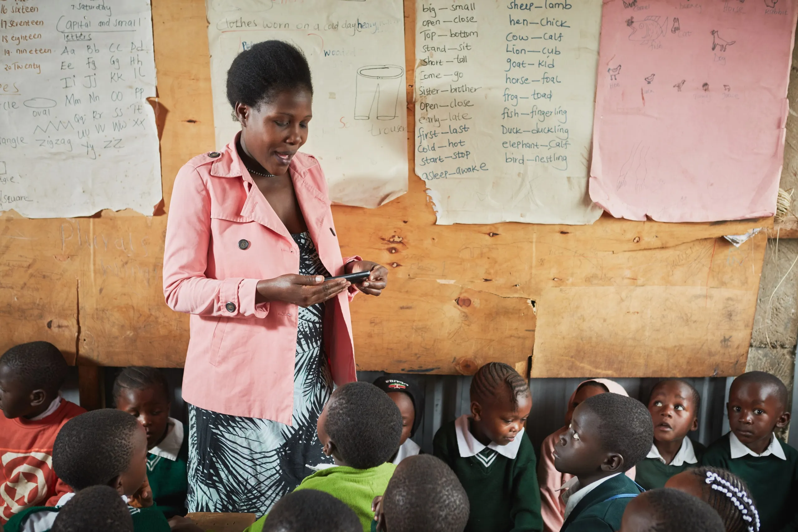 Teacher following a digital lesson plan on her phone, with pupils sitting on the floor around her