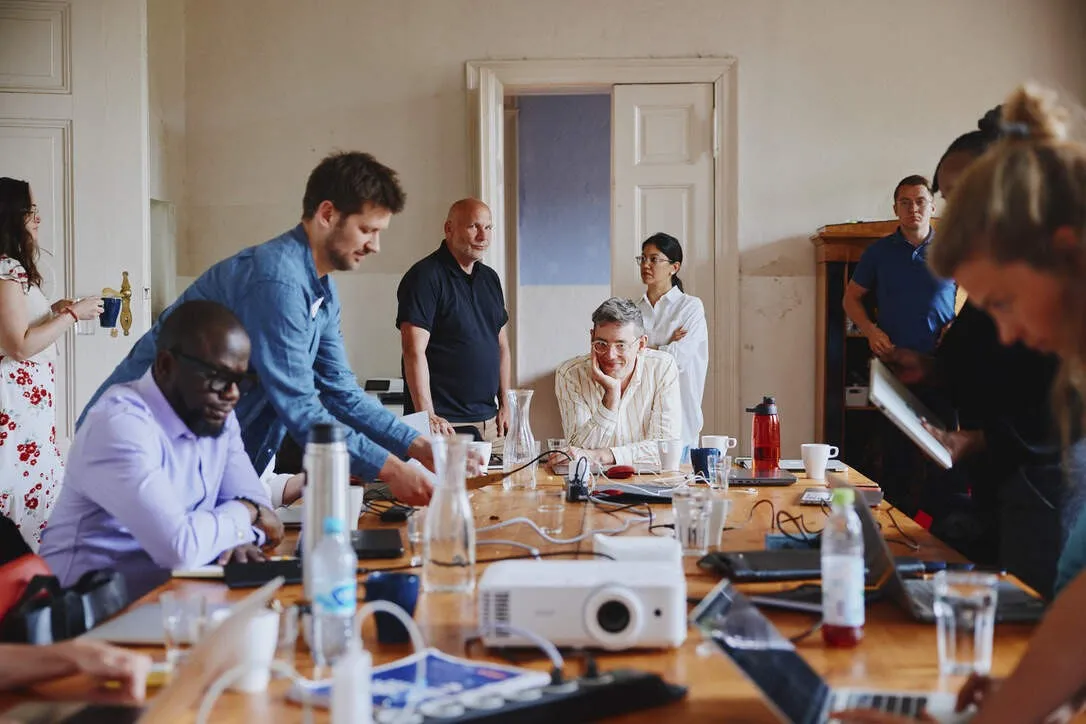 Team members working around a long table with laptops and a projector during an offsite