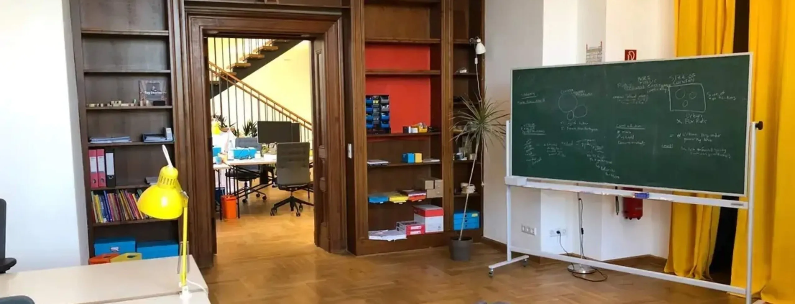 Berlin office with wood-panelled bookshelves, a yellow desk lamp and a chalkboard covered in notes