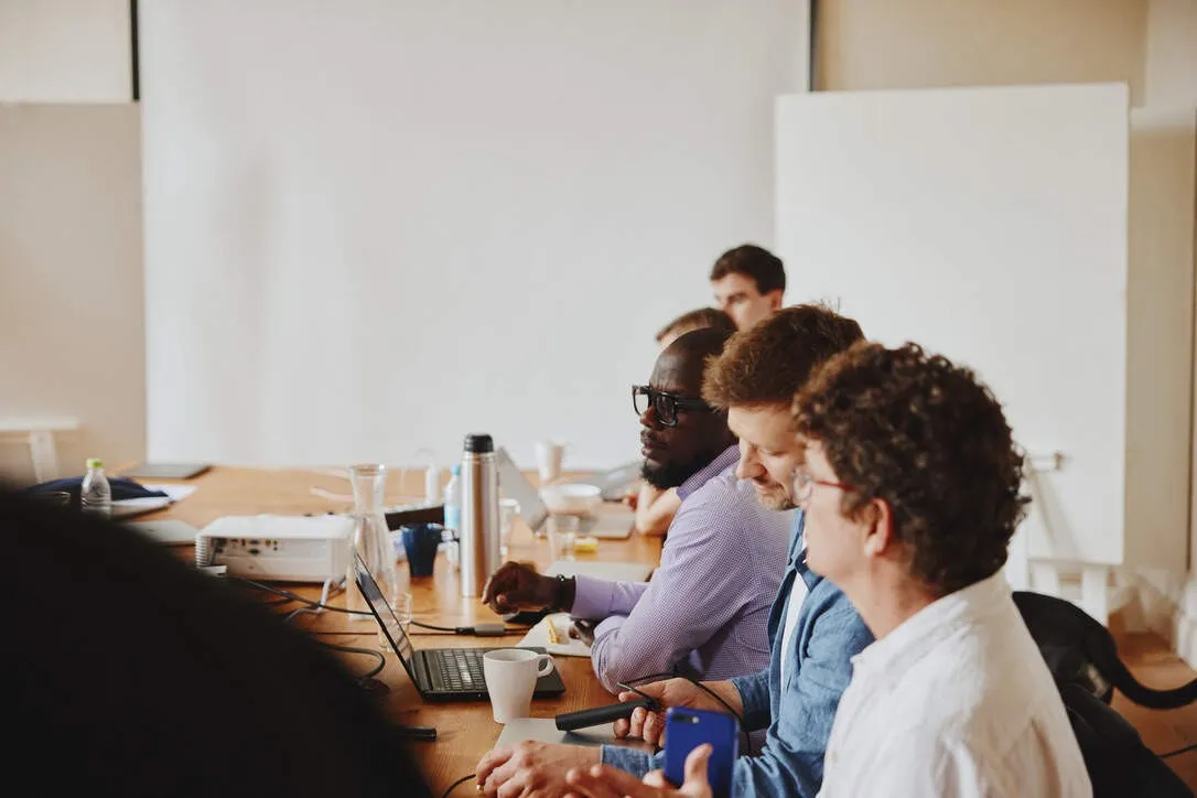 Colleagues listening and taking notes along a meeting table with laptops