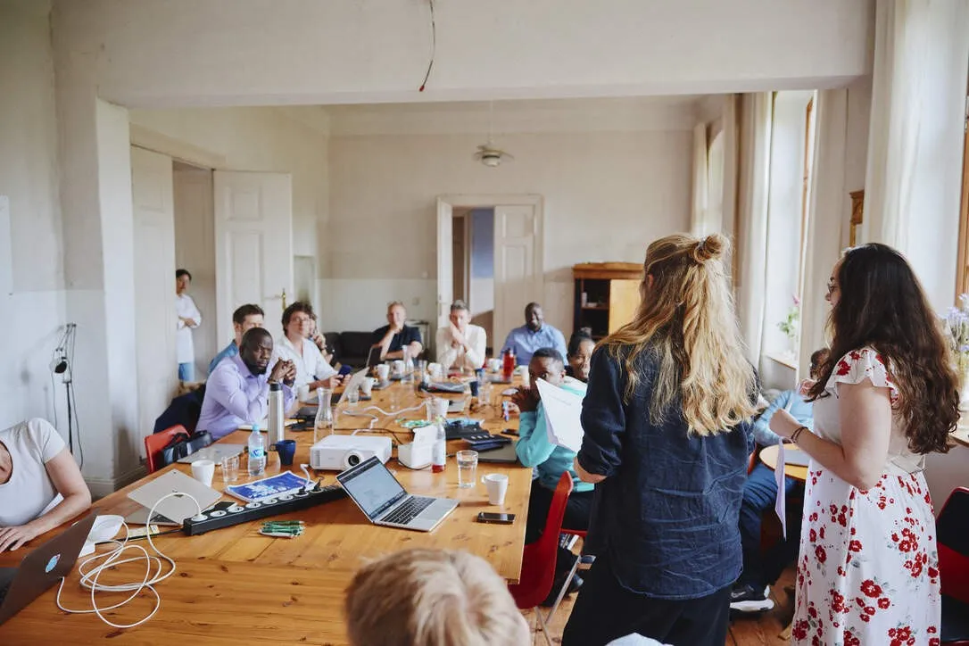 Two colleagues presenting to the team seated around a long table during an offsite
