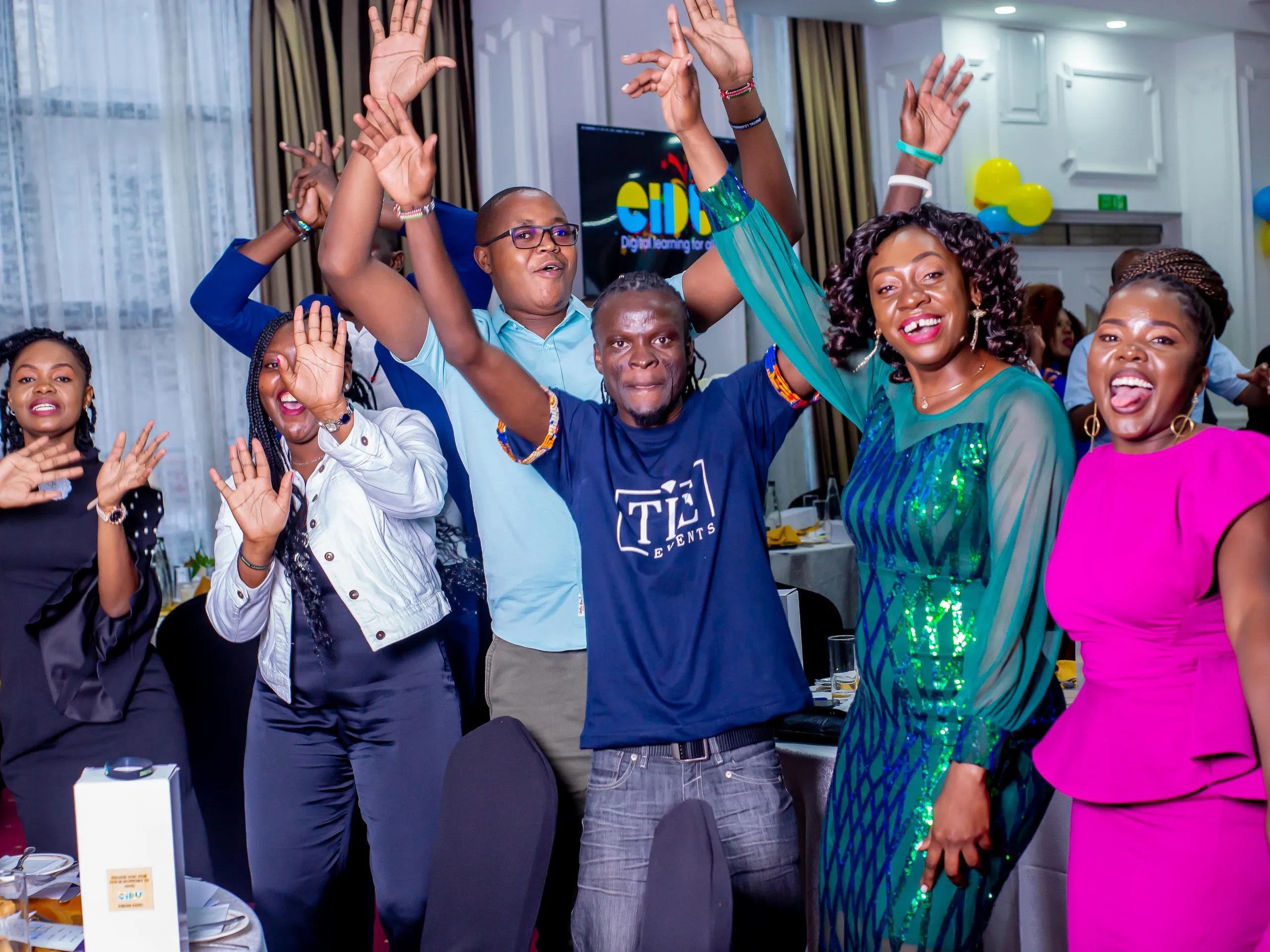 EIDU colleagues dancing with their arms up at a company party, in front of an EIDU screen