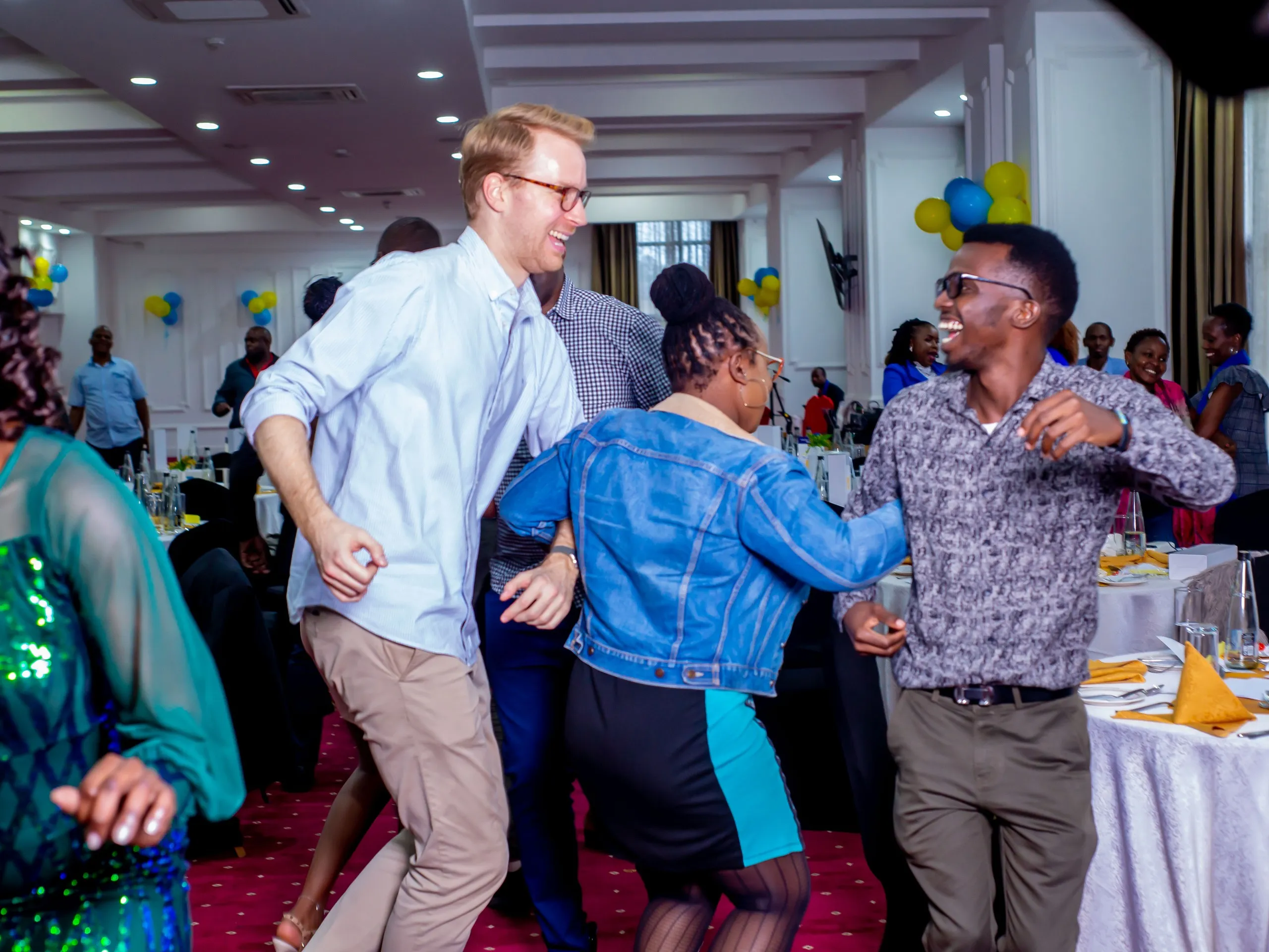 Colleagues dancing together at a company party decorated with blue and yellow balloons