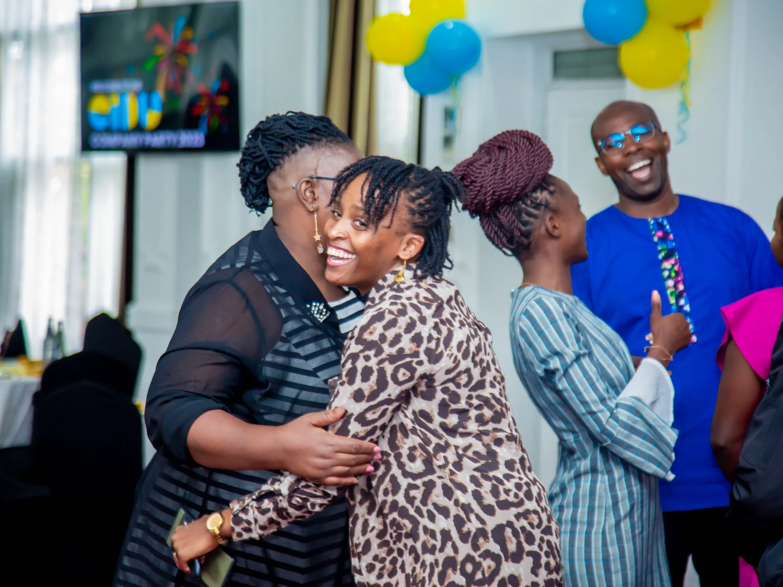 EIDU colleagues hugging and laughing at a company party with blue and yellow balloons