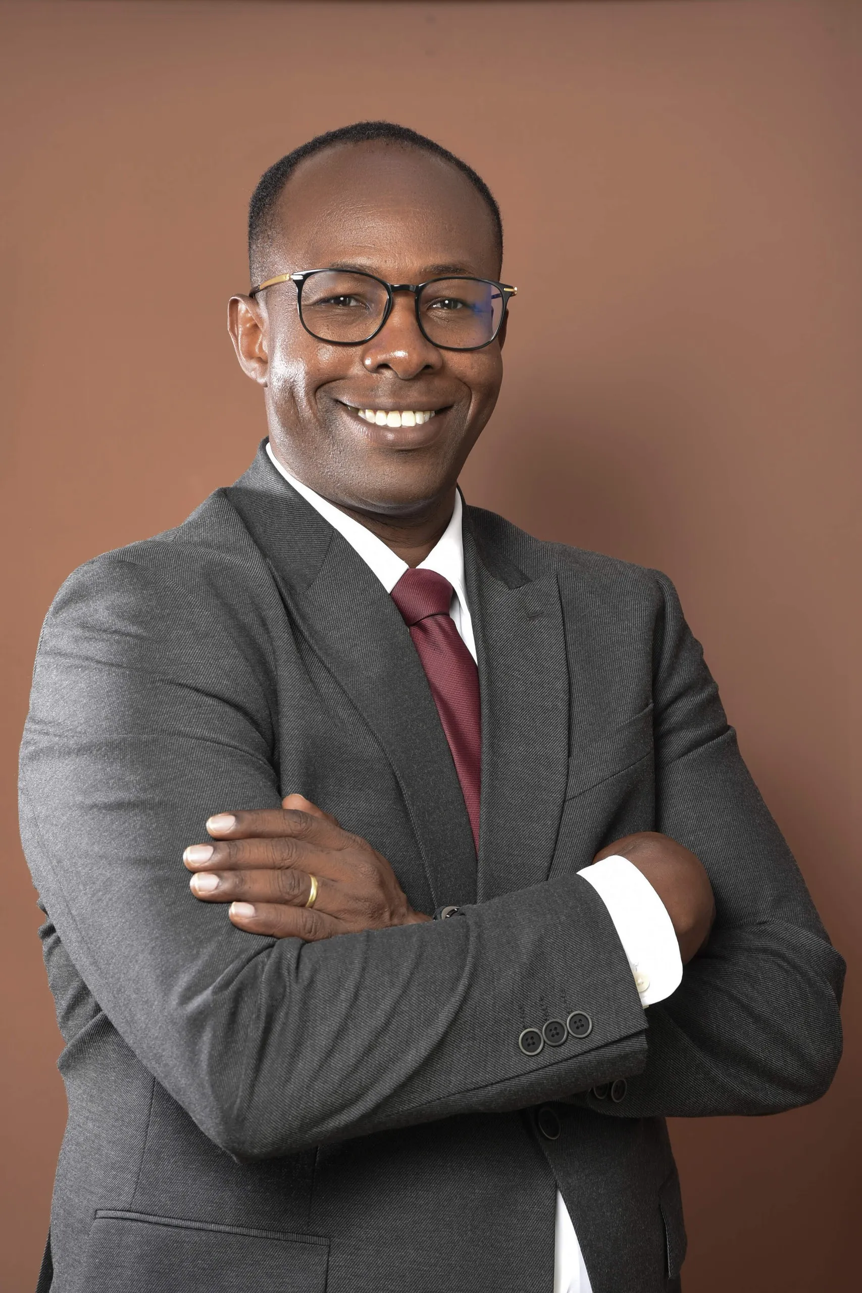 Fredrick Seda smiling with arms folded, wearing a grey suit and burgundy tie
