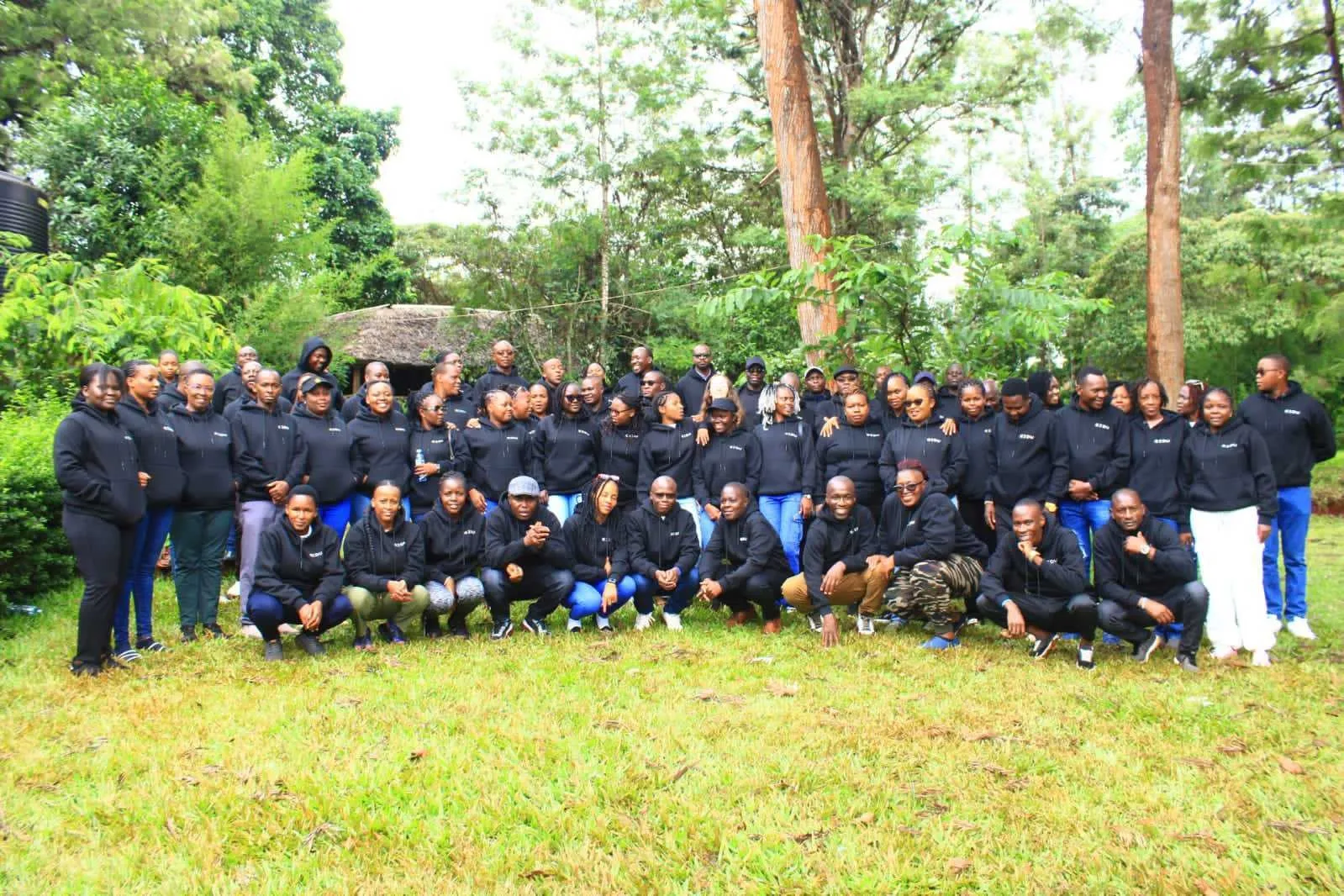 Large EIDU team posing outdoors among trees in matching black EIDU hoodies