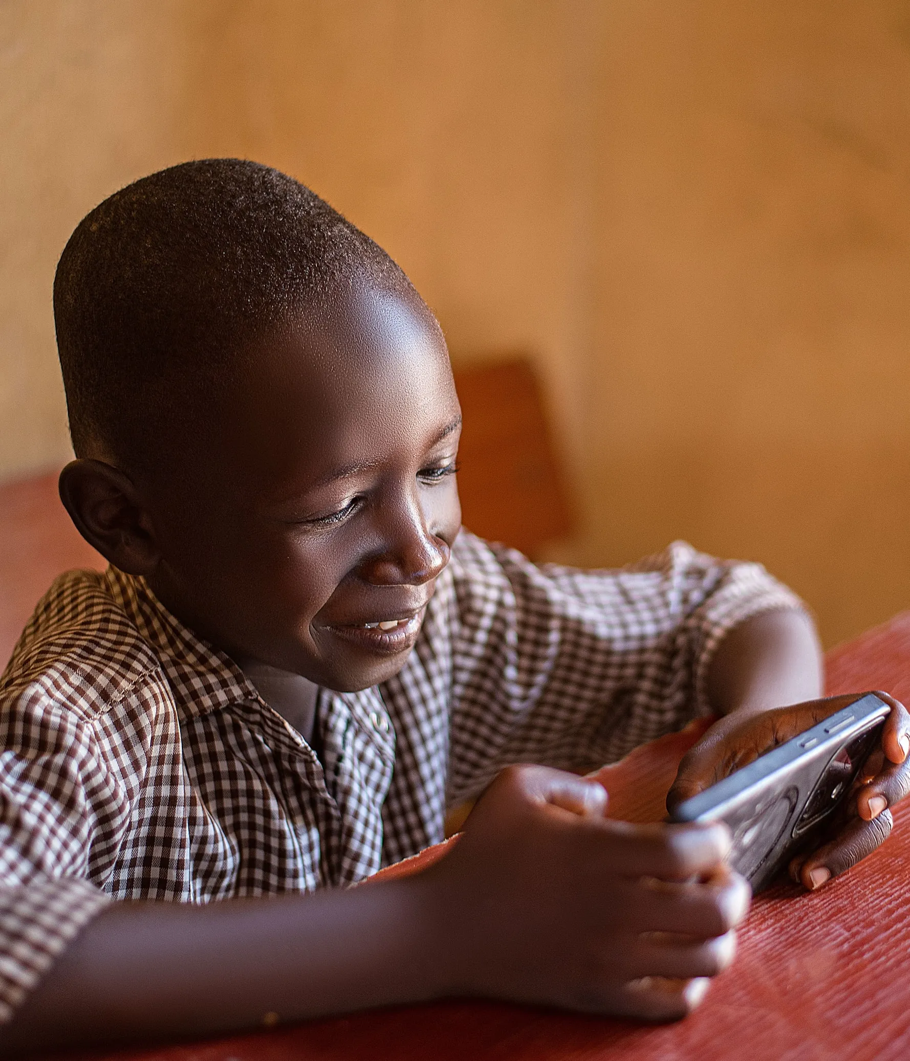 A boy smiling as he does a lesson on a phone in warm light, in Adamawa State, Nigeria