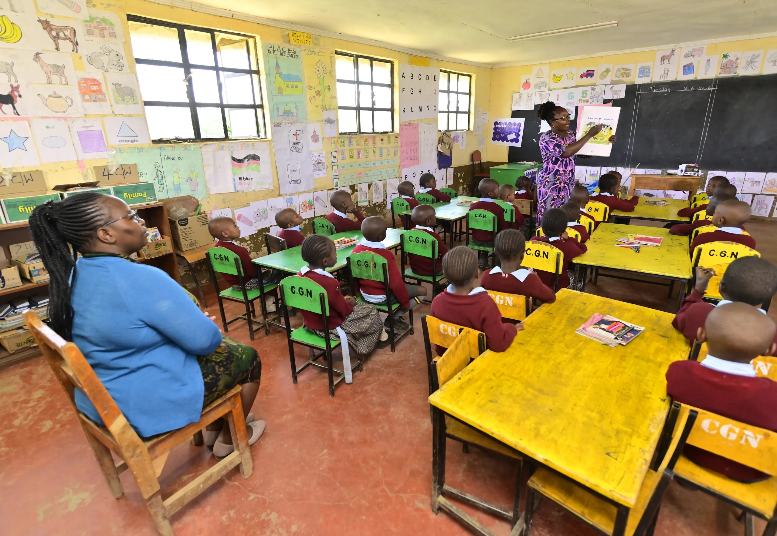Teacher reading a picture book to a pre-primary class in maroon uniforms while another teacher looks on