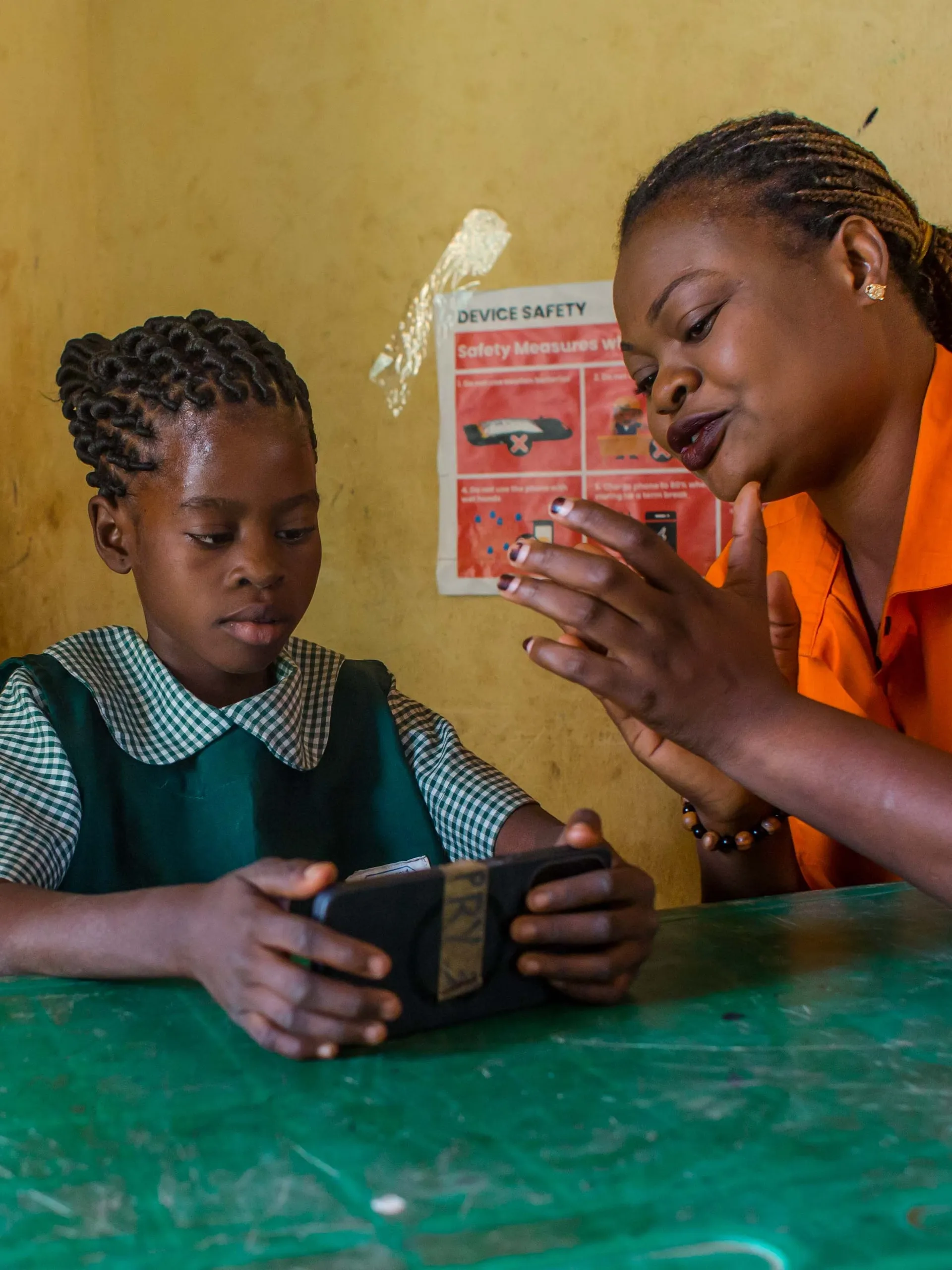 A teacher encouraging a girl as she does a lesson on a phone in Oyo State, Nigeria