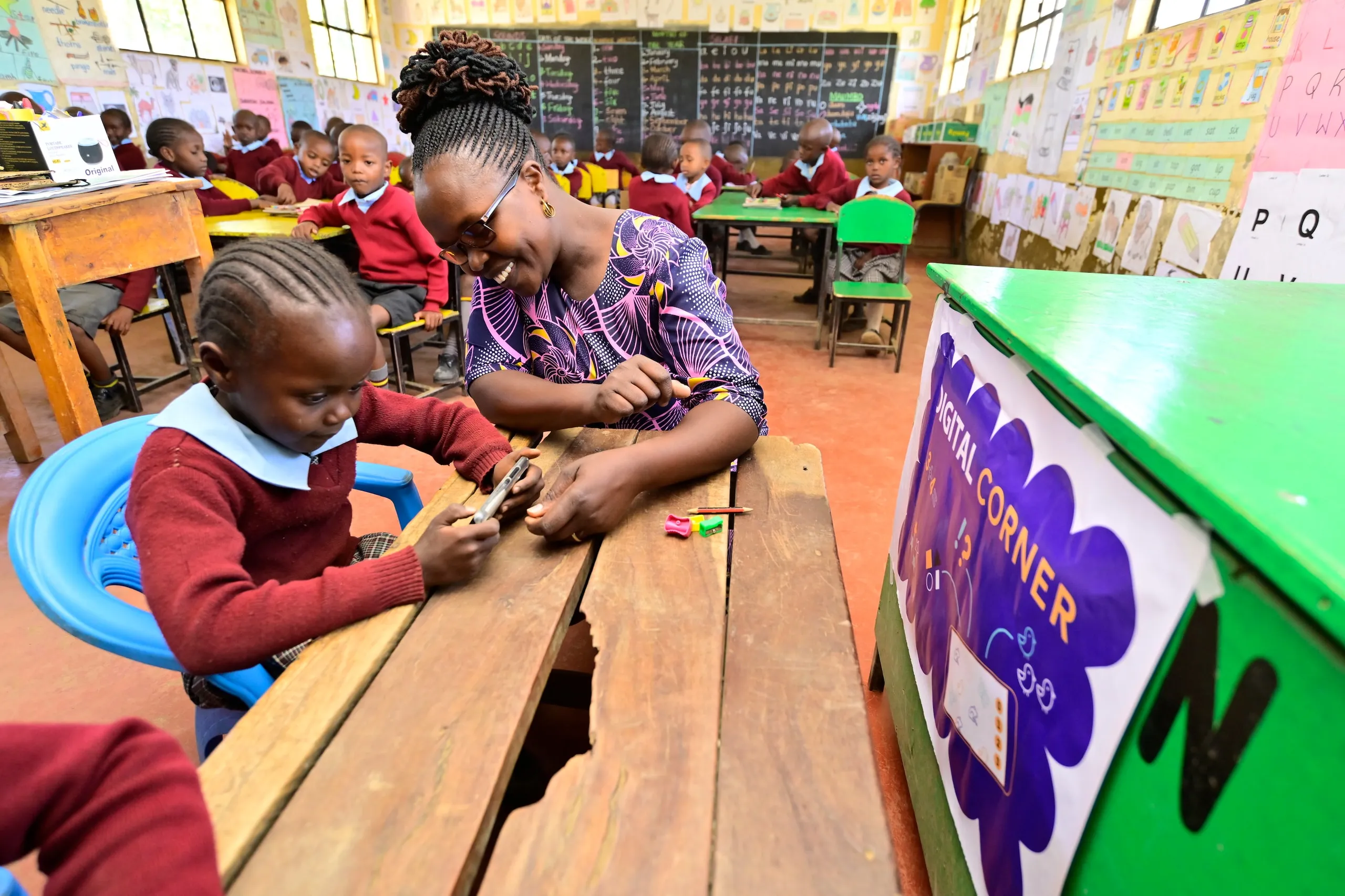 A teacher smiling as a girl works beside her at the digital corner of a classroom in Nakuru County, Kenya